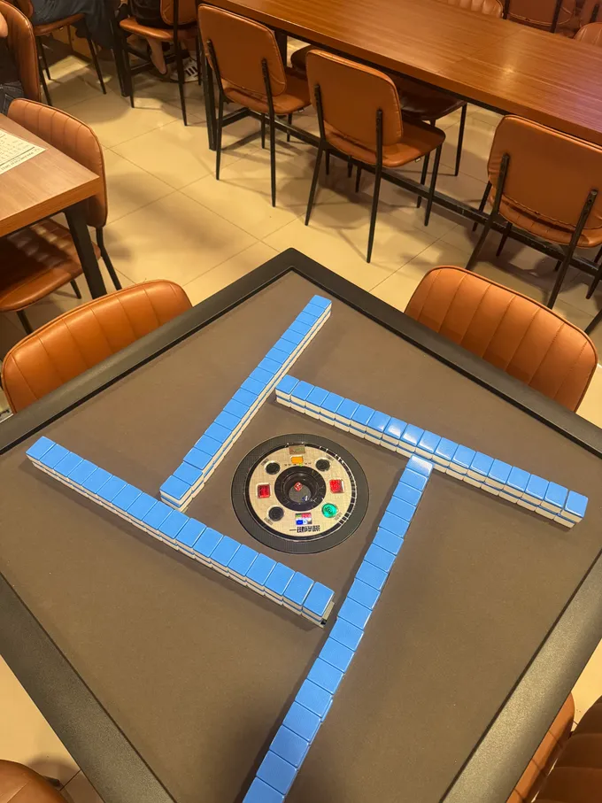 Meja mahjong otomatis di Gameopoly Gading Serpong — tile biru tersusun otomatis jadi empat tembok dengan panel kontrol dan dadu elektronik di tengah meja